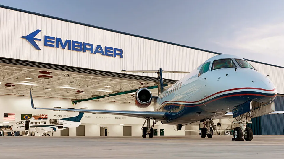 Jato da Embraer em frente a um hangar com a marca Embraer